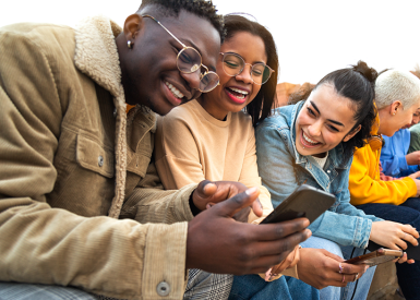 A group of multiracial youth joyfully gather to view content on their smart phones. Image source: Shutterstock.